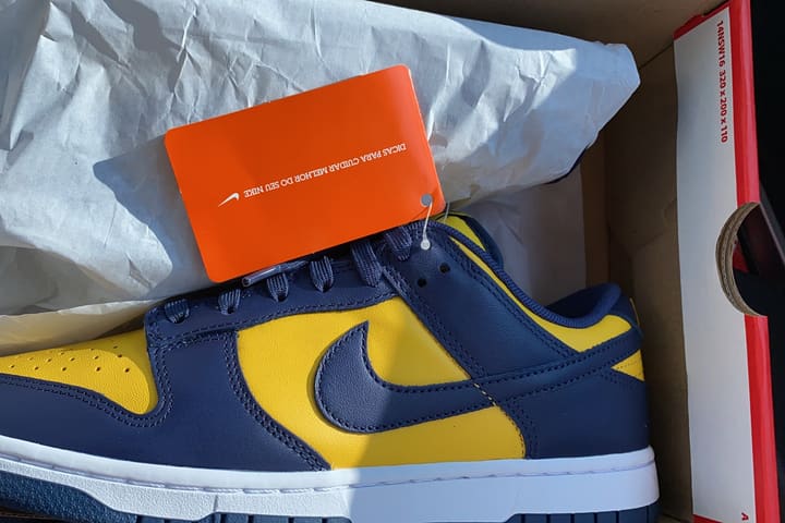A navy and yellow Nike Dunk Low in its box with the retail tag still attached.